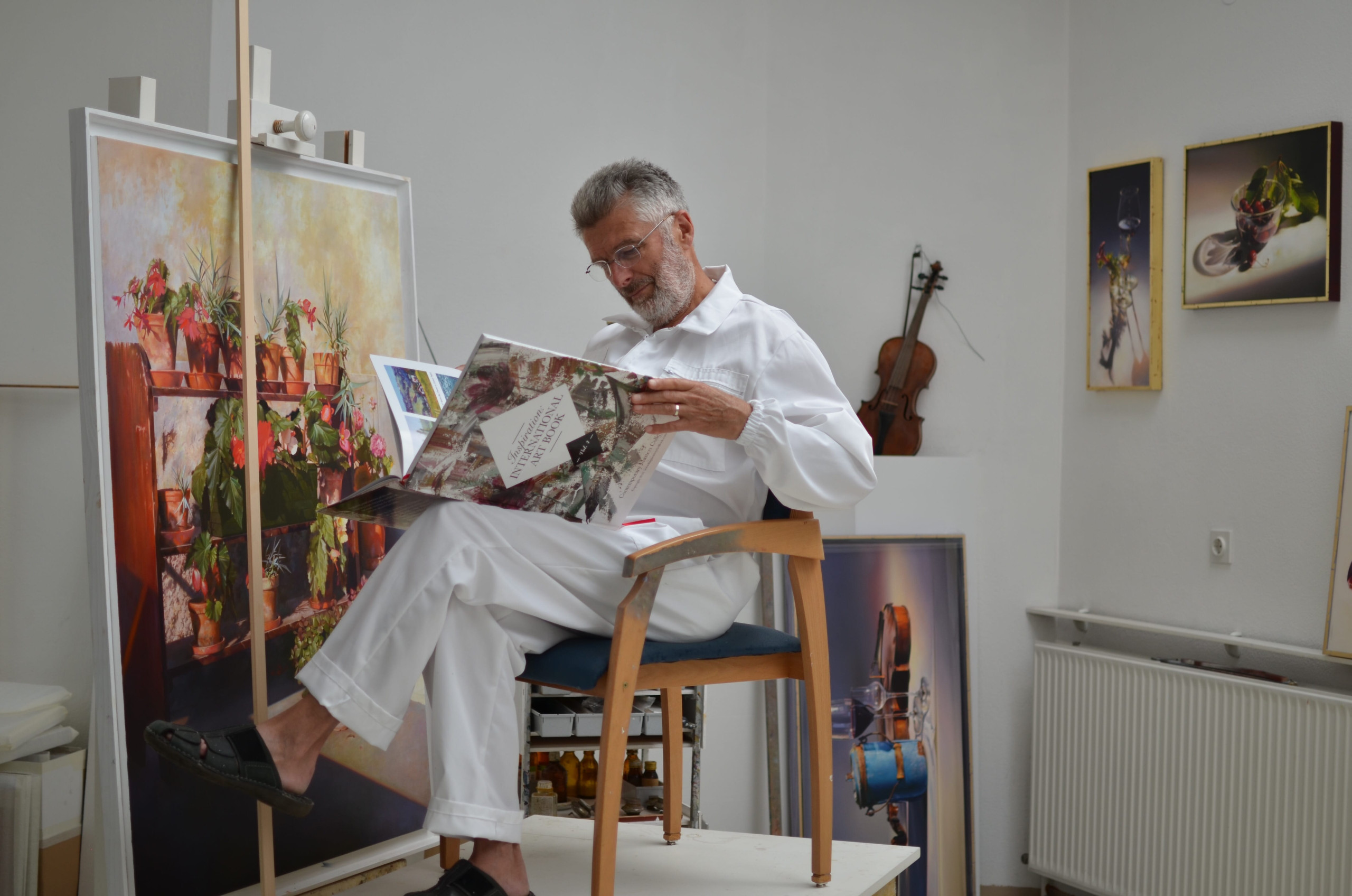 Pavel Florjančič in His Studio – Slovenian Painter of Still Life lovenian painter Pavel Florjančič sitting in his studio, reading an art book beside one of his still life oil paintings.