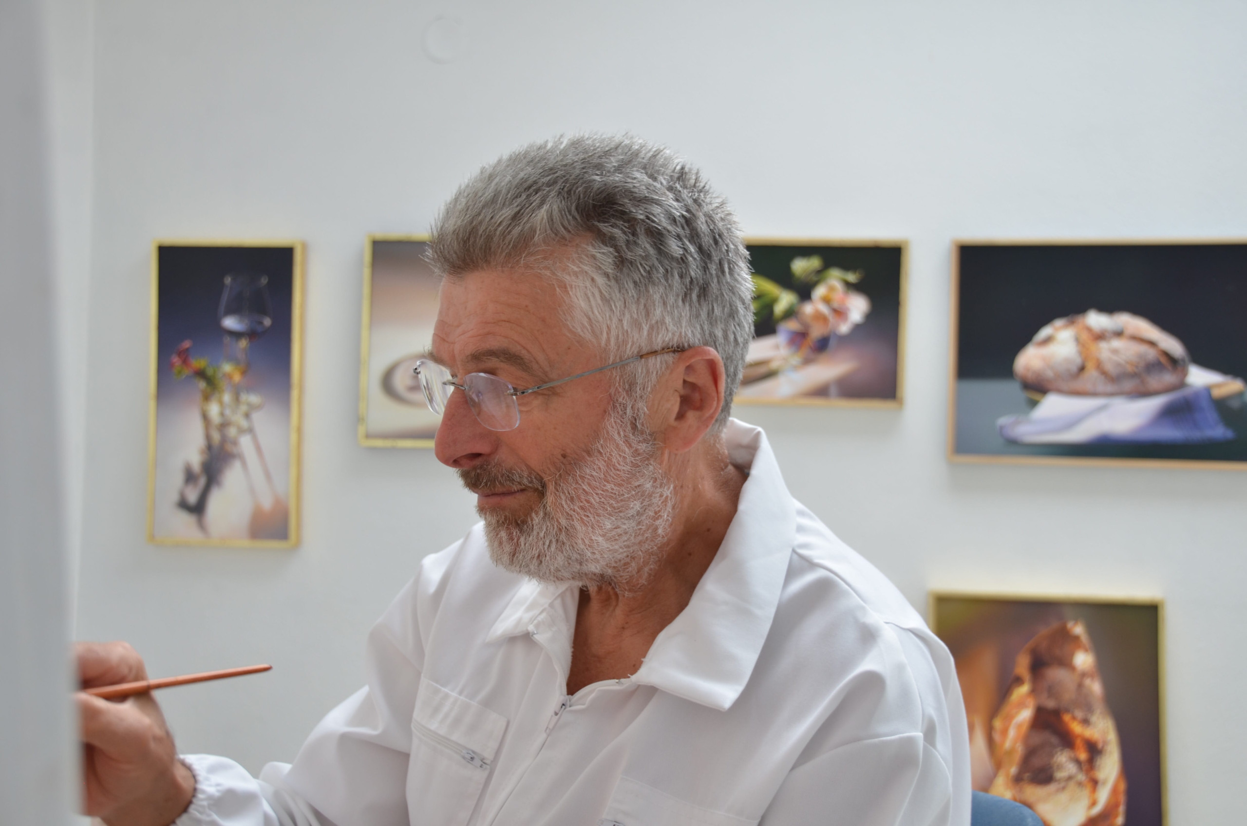 Pavel Florjančič focused on painting in his studio, surrounded by framed still life artworks.